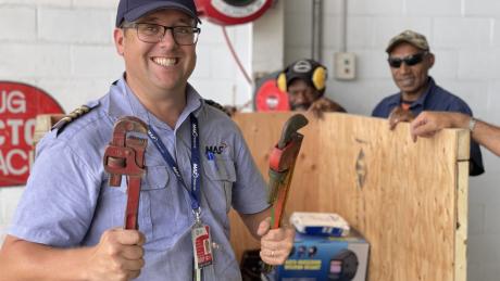 Pilot Tim Neufeld with some tools in front of the crate, while two other workmen are standing in the back