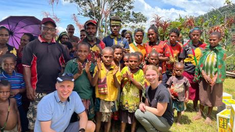 Stephanie Hald and David Berscheminski sits with a group of locals from Megau under the wing of the MAF aircraft