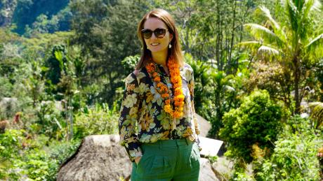 A woman with a lei smiles in a PNG village setting