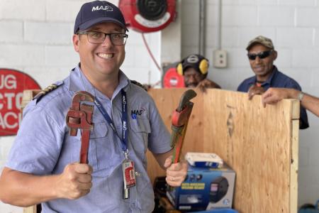 Pilot Tim Neufeld with some tools in front of the crate, while two other workmen are standing in the back