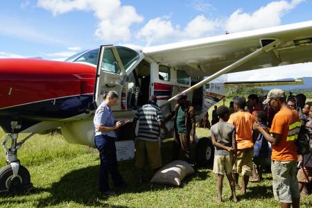 MAF Pilot Glenys Watson looking at flight paperwork as her plane gets loaded by locals.