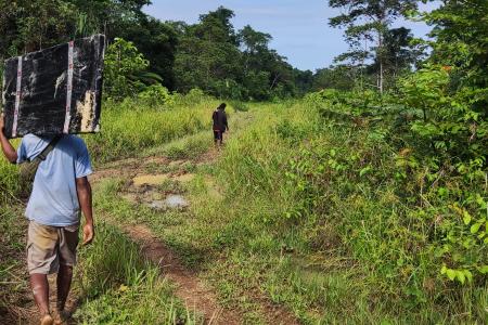 A Male carrying a solar panel while working on a muddy road heading into the remote community of Wasengla
