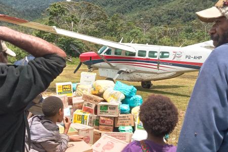 People watch an MAF plane taxi away as they stand by their goods received