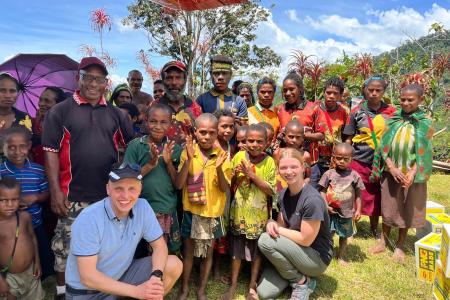 Stephanie Hald and David Berscheminski sits with a group of locals from Megau under the wing of the MAF aircraft