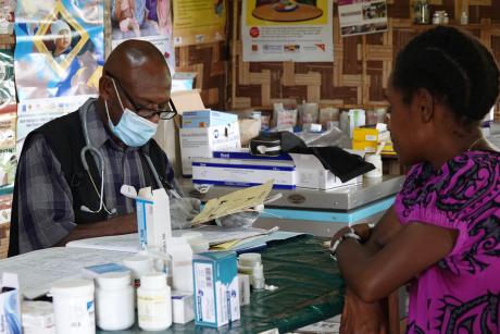 Jamie on his desk writing into the medical record book of a patient sitting across from him