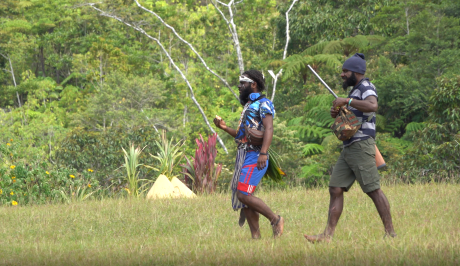 Two men walking, one holding a rifle.