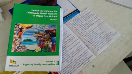 school book used by the CHW school next to a student's notes